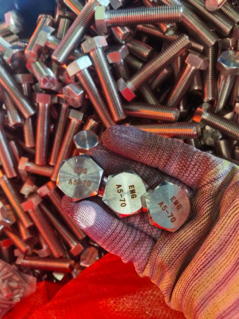 Gloved hand presenting three hex cap screw heads with visible EMG A5-70 markings